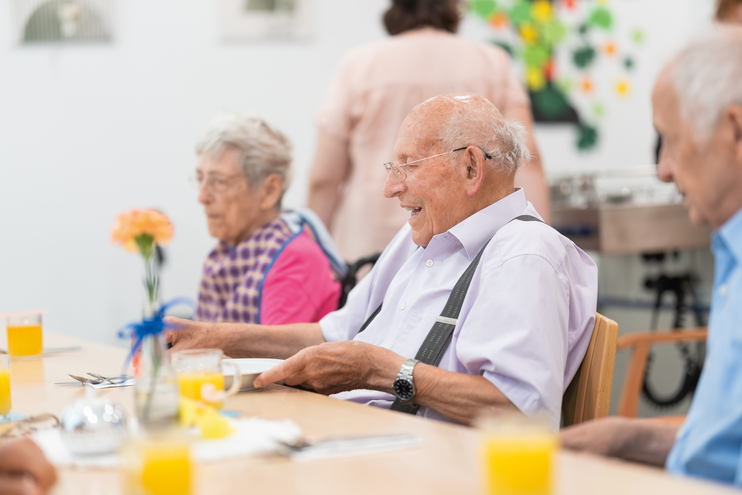Älterer Herr sitzt gemeinsam mit anderen Menschen an einem Esstisch