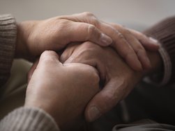 Die Hände einer Person halten die Hand einer anderen, älteren Person.