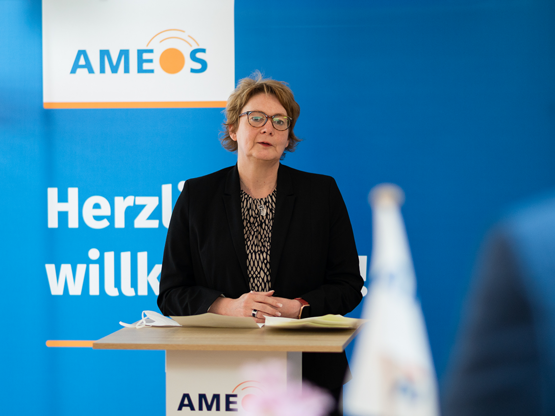 Ministerin Daniela Behrens an einem Rednerpult vor blauem Hintergrund mit AMEOS Logo