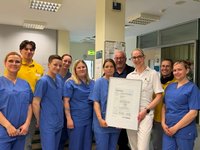 Pflegepersonal und ärztliches Personal auf der Regionalen Stroke Unit hält lächelnd ein Zertifikat in die Kamera.