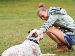 Eine Rehabilitandin zusammen mit ihrem Hund beim Hundetraining. Sie streichelt ihren Hund und lächelt fröhlich.