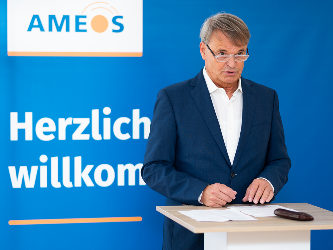 AMEOS Vorstand Michael Dieckmann an einem Rednerpult vor blauem Hintergrund mit AMEOS Logo