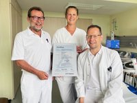 Zwei Ärzte und eine Schwester halten das Zertifikat und lächeln.