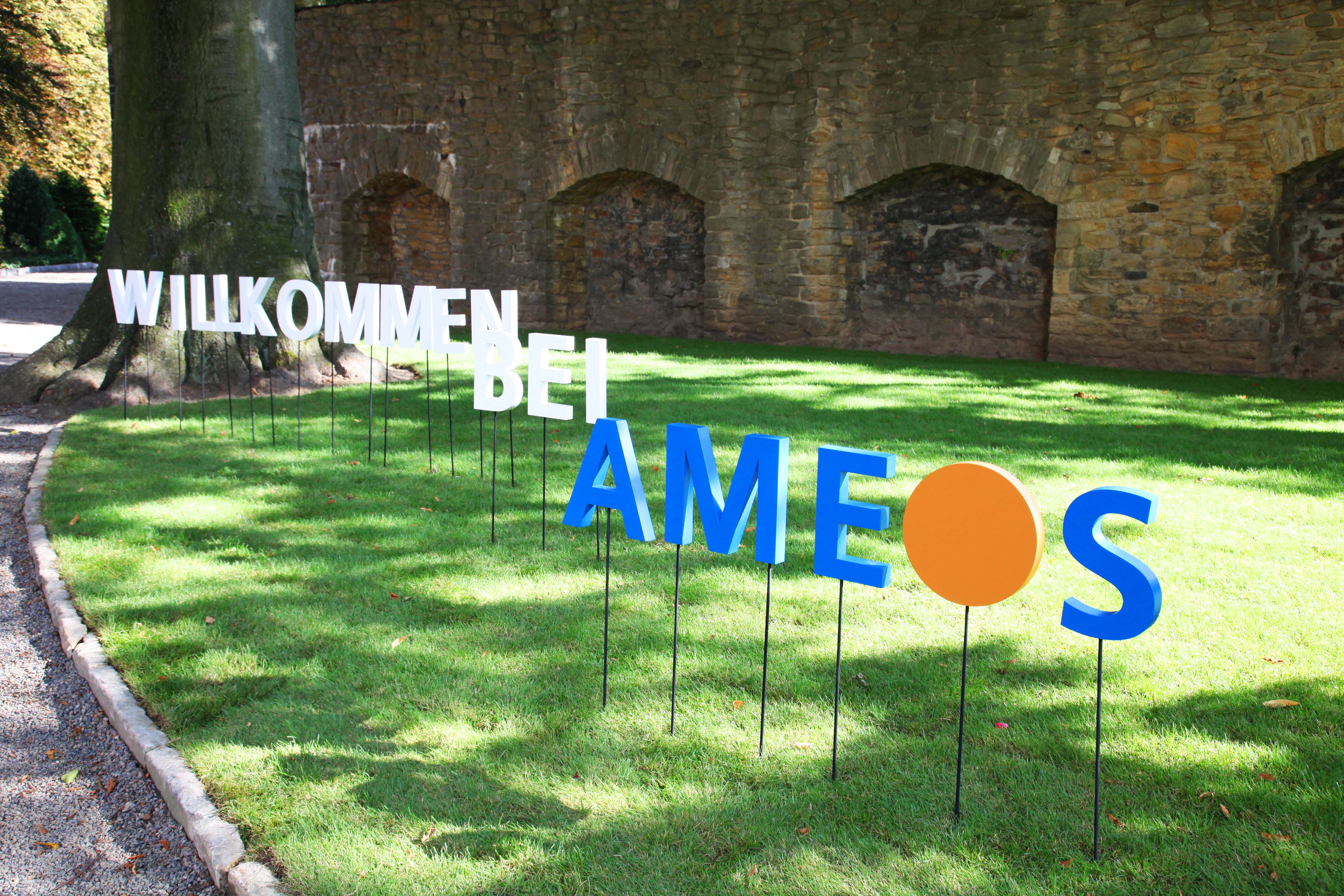 Auf einer Wiese ist der Schriftzug "Willkommen bei AMEOS" zu sehen